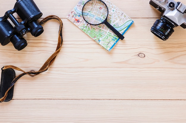 Free photo elevated view of binoculars; magnifying glass; map and camera on wooden surface