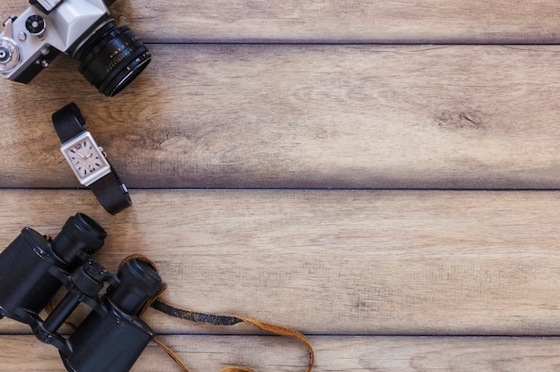 Free photo elevated view of binoculars; wrist watch and camera on wooden backdrop