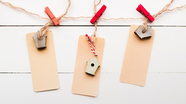 Free photo an elevated view of birdhouse tag tied with cloth pegs on white wooden plank