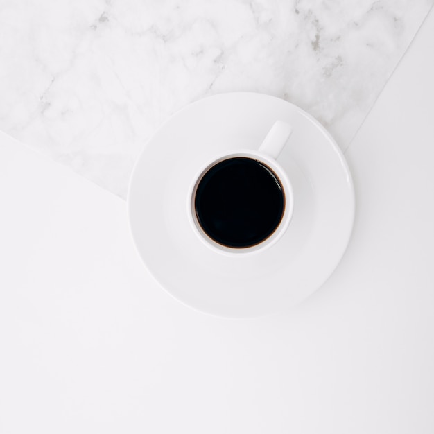 Free photo an elevated view of black coffee cup on saucer over the marble and white background