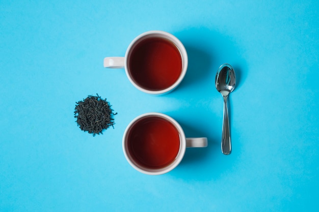 Free Photo an elevated view of black herbal tea cups and spoon on blue background