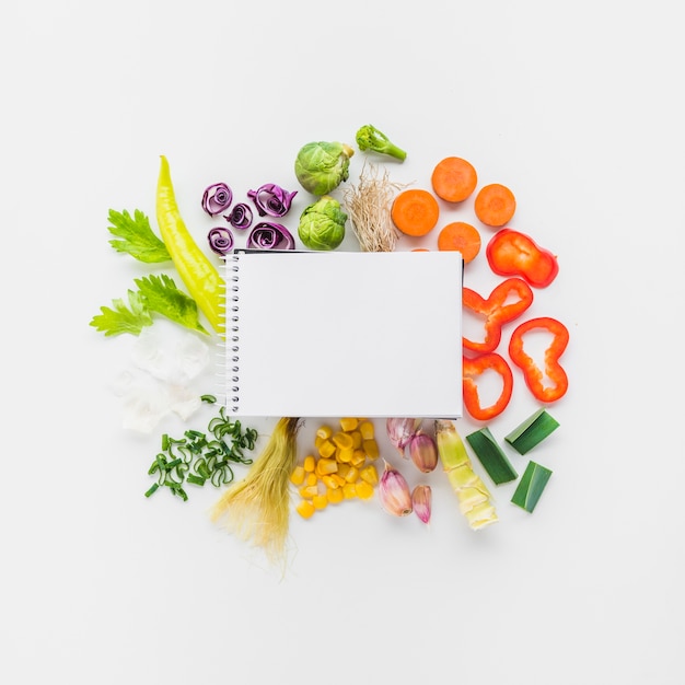 Free photo elevated view of blank spiral notepad on fresh vegetables over white background