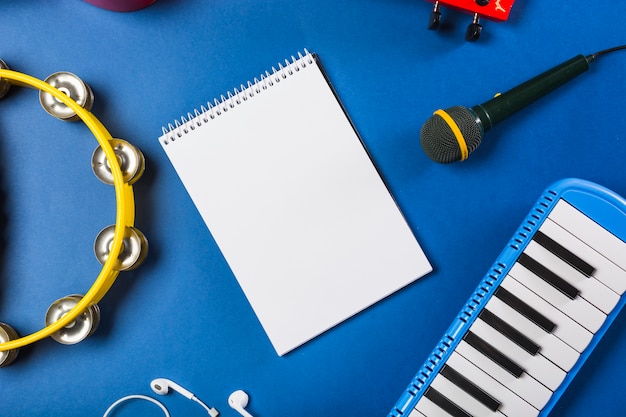 Free Photo elevated view of blank spiral notepad with earphone; guitar; microphone; piano keyboard and tambourine over blue background