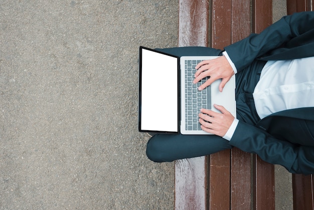 Free photo an elevated view of businessman sitting on bench typing on laptop