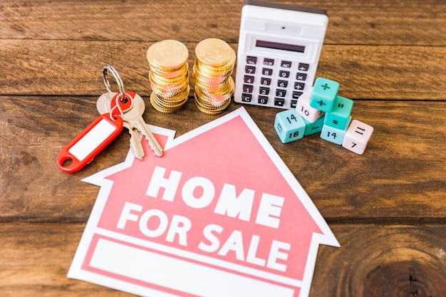 Elevated view of calculator, math blocks, stacked coins and key with home for sale icon