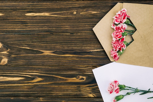 Free photo elevated view of carnation flowers in envelop on brown table