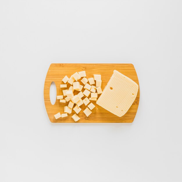 An elevated view of cheese cubes on wooden chopping board over white background