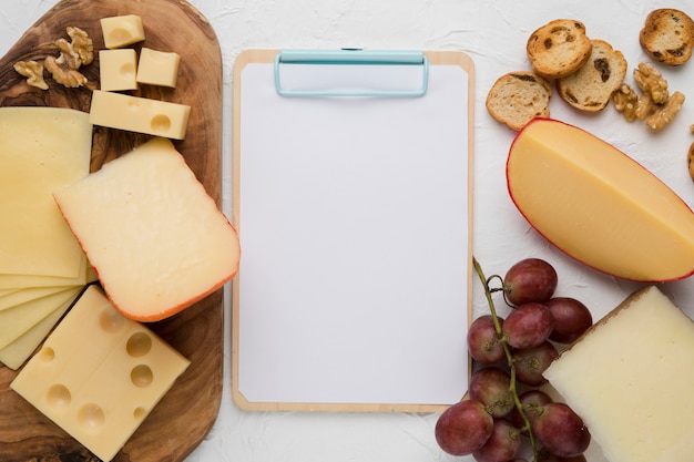 Free photo elevated view of cheese platter; walnut; red grapes and bread slice with empty clipboard