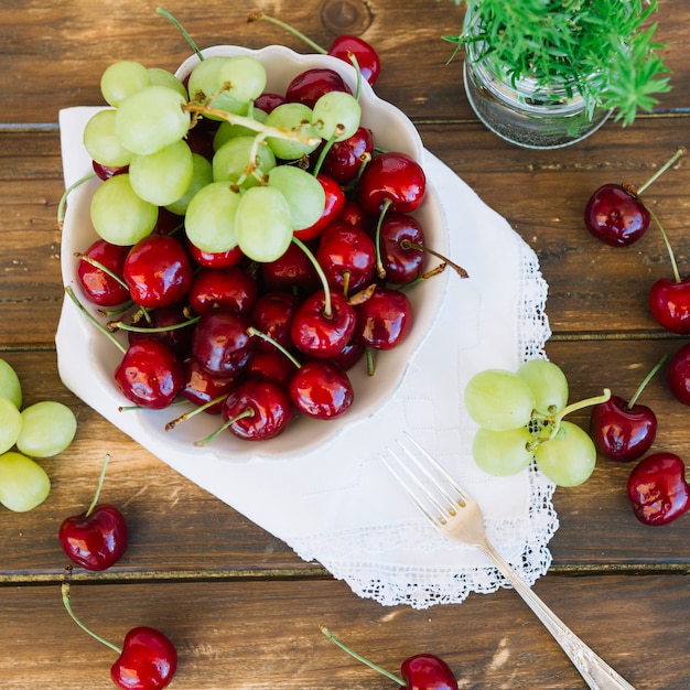 Free photo elevated view of cherries and grapes in bowl on wooden plank