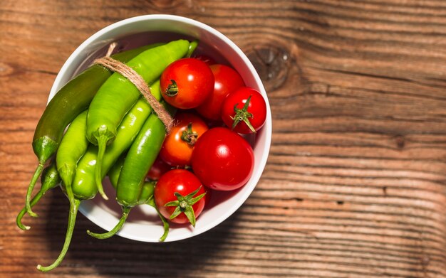 Elevated view of cherry tomatoes and green chili peppers on wooden surface