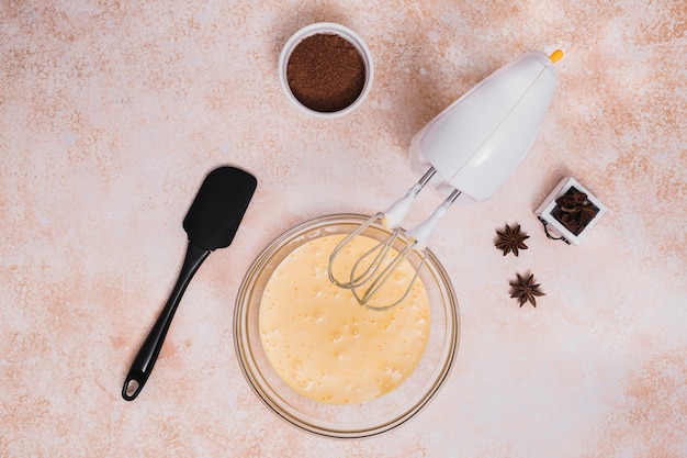 An elevated view of cocoa powder; spatula; star anise and mixed cake dough in glass bowl