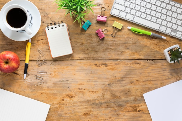 An elevated view of coffee cup; apple and office stationeries on wooden desk