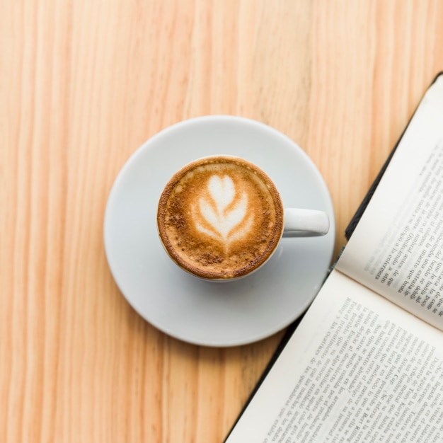 Elevated view of coffee latte and open book on wooden background