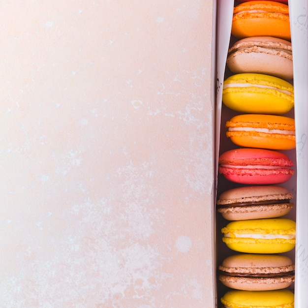 An elevated view of colorful macaroons in box on textured backdrop