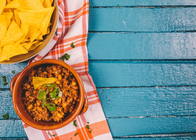 Free photo elevated view of cooked ground beef in bowl with mexican nachos chips on blue wooden desk