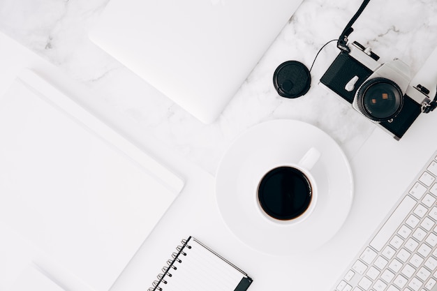 An elevated view of diary; digital tablet; coffee cup; camera and keyboard on desk