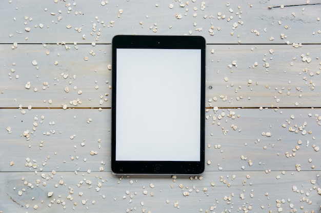 Free photo elevated view of digital tablet with scattered oats on wooden plank