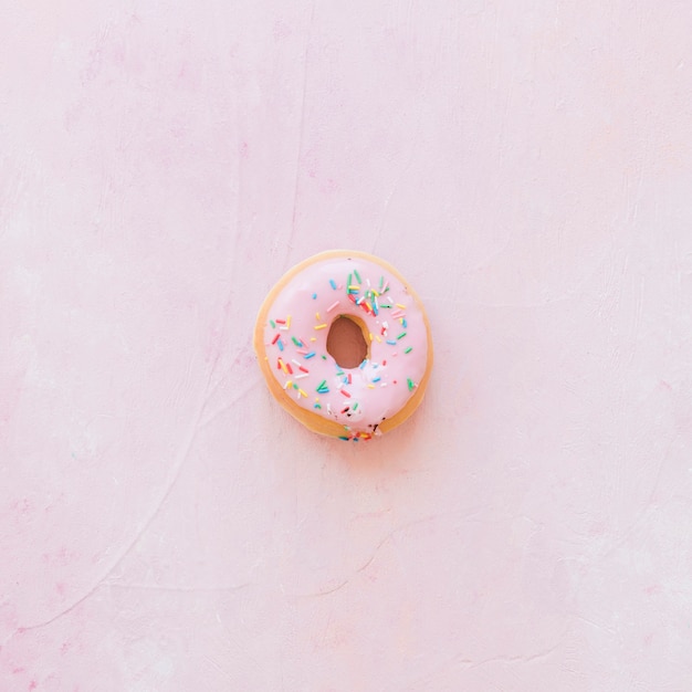 Elevated view of donut with sprinkles on pink backdrop