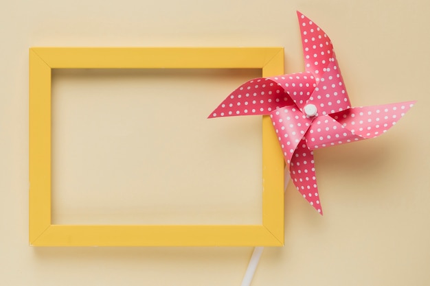 Free photo elevated view of dotted pinwheel and yellow frame on beige background