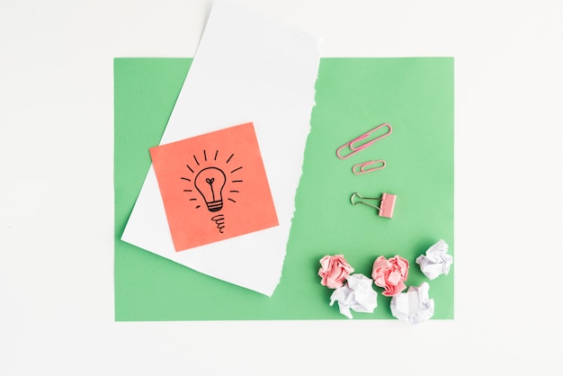 Elevated view of drawn light bulb and crumpled paper with paper clip on green card paper