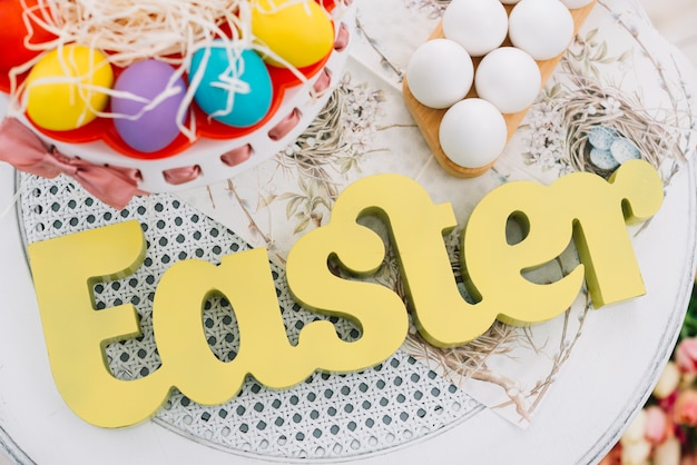 Free photo an elevated view of easter text with decorative colorful easter eggs on white table