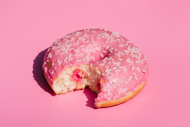 An elevated view of eaten donut on pink background