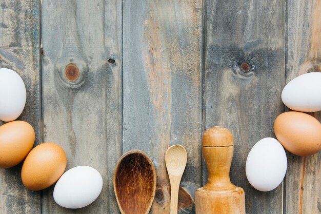 Elevated view of eggs with rolling pin and spoon on wooden backdrop