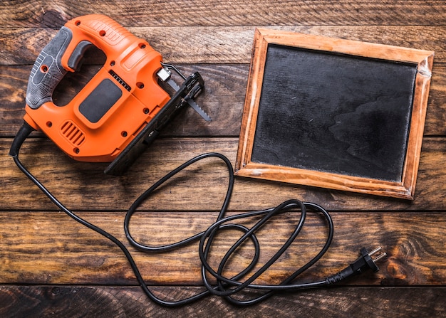 Free photo elevated view of electric jigsaw and blank slate on wooden background