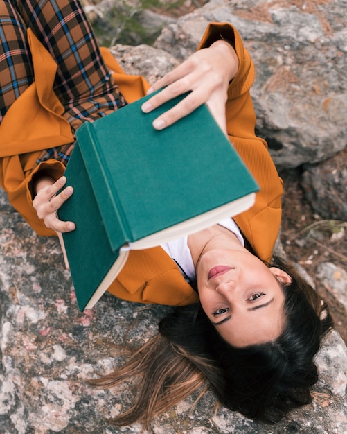 Free Photo an elevated view of a female hiker relaxing on rock reading the book