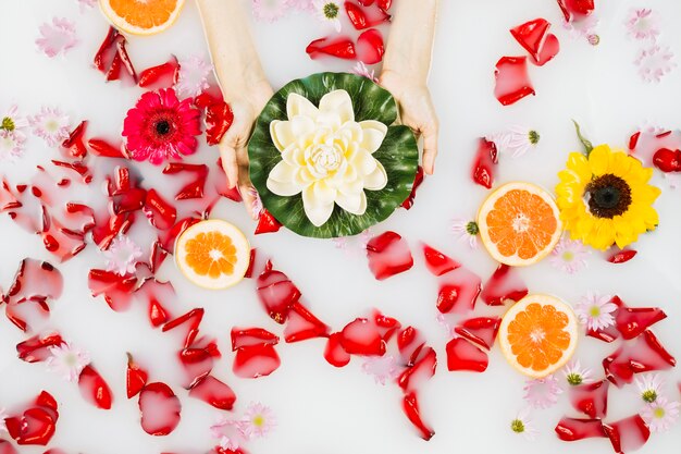 Elevated view of female's hand holding lotus and decorated spa bath with milk