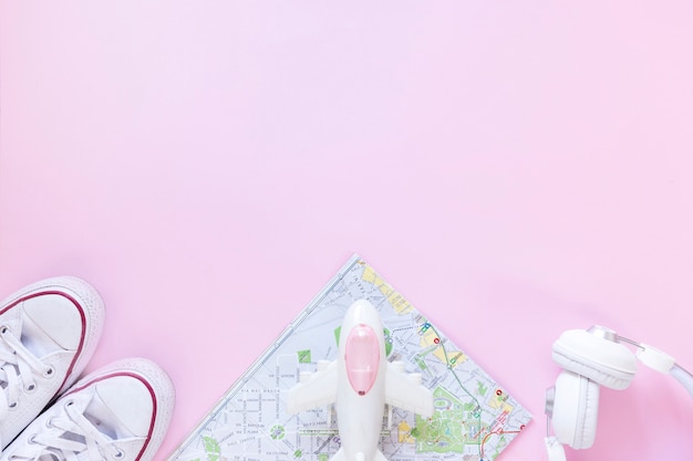 Elevated view of footwear; map; airplane and earphone on pink background