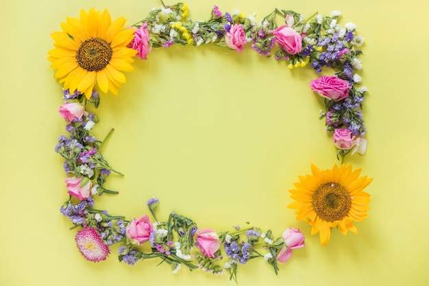 Elevated view of fresh flowers forming frame on yellow surface