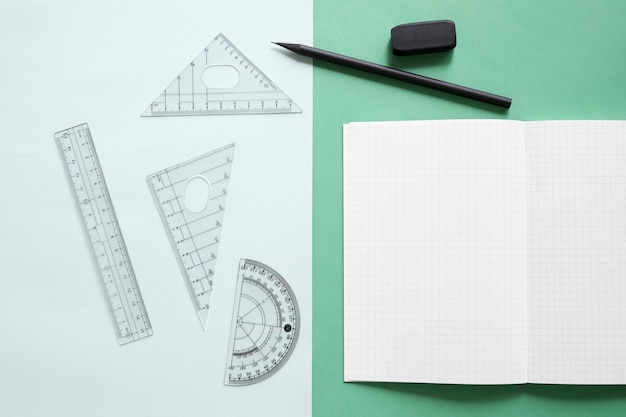 Elevated view of geometric equipment; notebook; pencil and eraser on dual colorful background