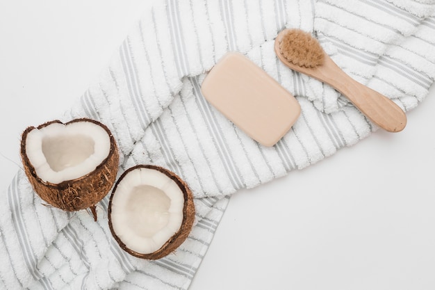 Free Photo elevated view of halved coconut; towel; soap and brush on white backdrop