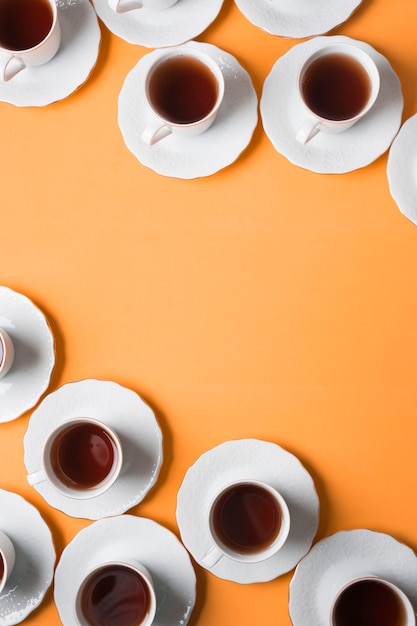 Free photo an elevated view of herbal tea cup and saucers on the corner of an orange background