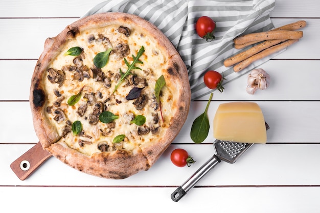 Elevated view of homemade mushroom pizza and bread sticks with ingredients on white plank