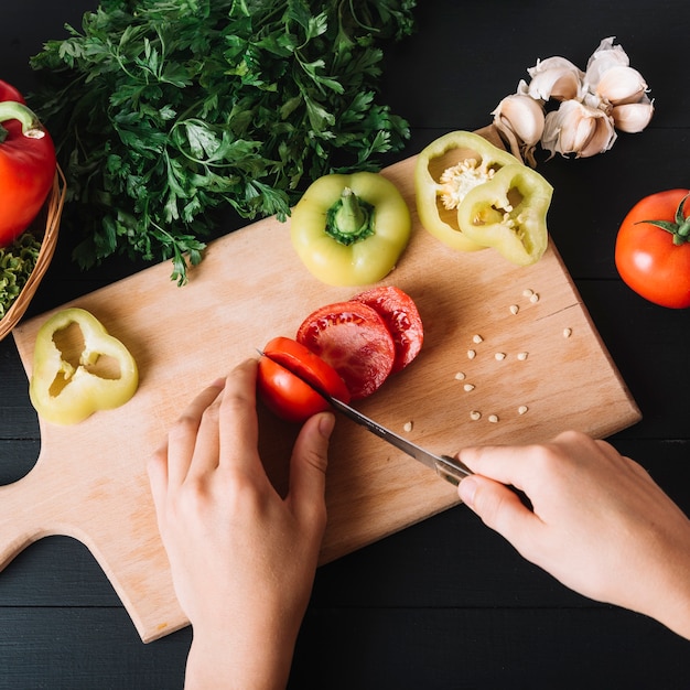 Free Photo elevated view of a human hand slicing fresh red tomato on wooden chopping board