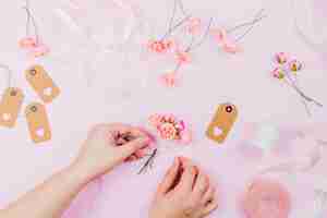 Free photo an elevated view of human hand tying the artificial flowers with ribbon on pink background