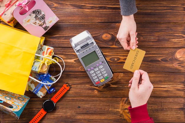 Elevated view of human hands holding gold card with swiping machine on wooden table