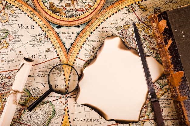 Free Photo elevated view of magnifying glass, burnt paper and knife on map