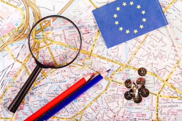 Free photo elevated view of magnifying glass, pushpins, pencils and flag on map