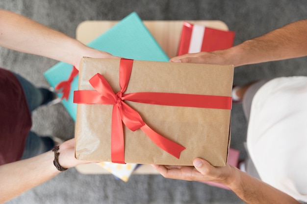 Elevated view of male friend's holding wrapped gift box with red ribbon bow