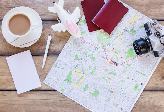 Free photo elevated view of passport; map; airplane; camera; paper and tea cup on wooden background