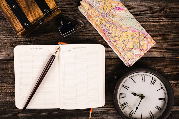 Free photo elevated view of pen, diary, map and clock on wooden background