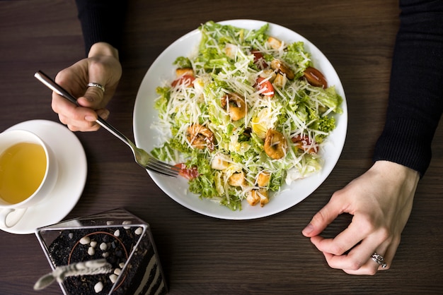 Elevated view of a person having caesar salad with shrimp on white plate over table