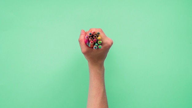 Elevated view of a person's hand holding group of colorful pencils on green background