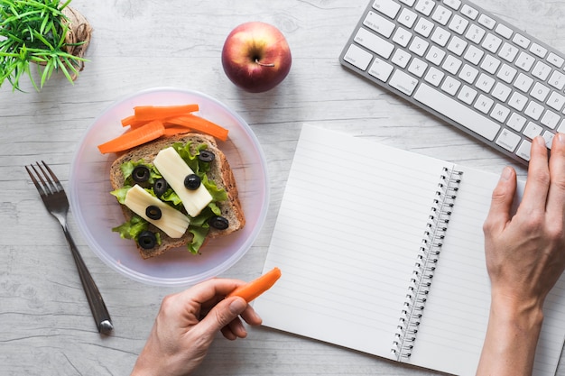 Free photo elevated view of person's hand holding healthy food while working on keyboard