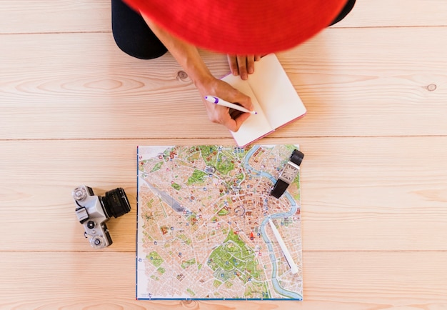 Free Photo elevated view of person writing in diary with map; wrist watch and camera on wooden table