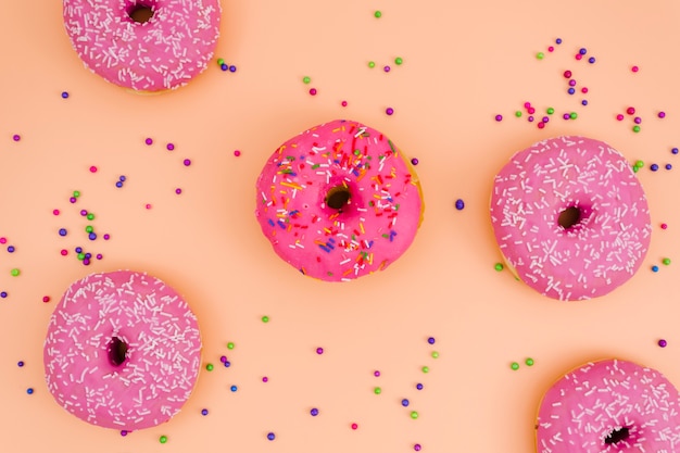 An elevated view of pink donuts with sprinkles balls on colored backdrop