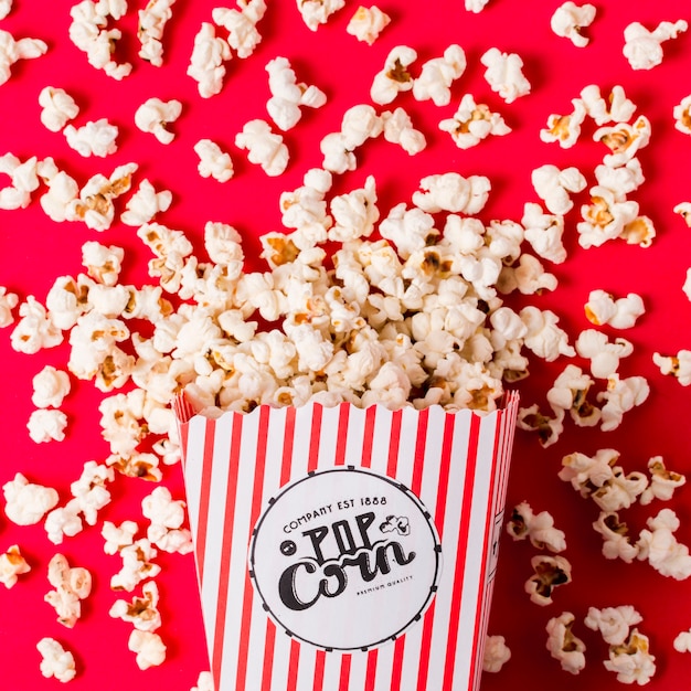 An elevated view of popcorns spilled from the striped box on red backdrop